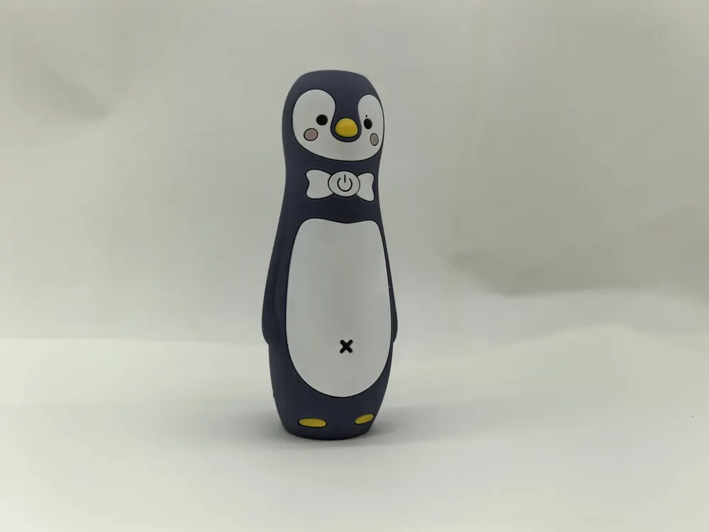 Dark navy silicone figure moulded as a penguin, with a printed white belly, printed eyes and yellow moulded feet.